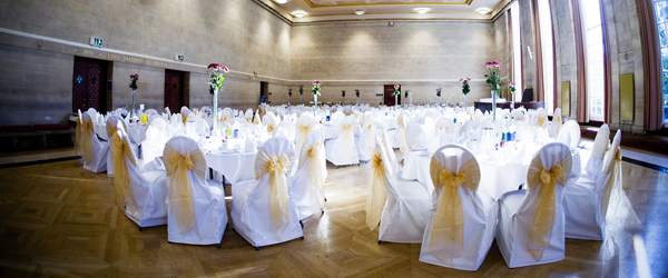 a room set up cabaret style for a wedding reception with yellow bows on the backs of the chairs