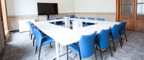 a spacious bright meeting room with a large white table and blue chairs