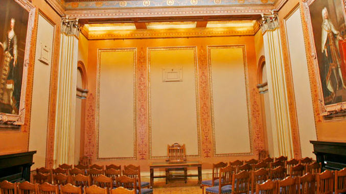 A high ceilinged room with large paintings on the walls set up for a wedding ceremony