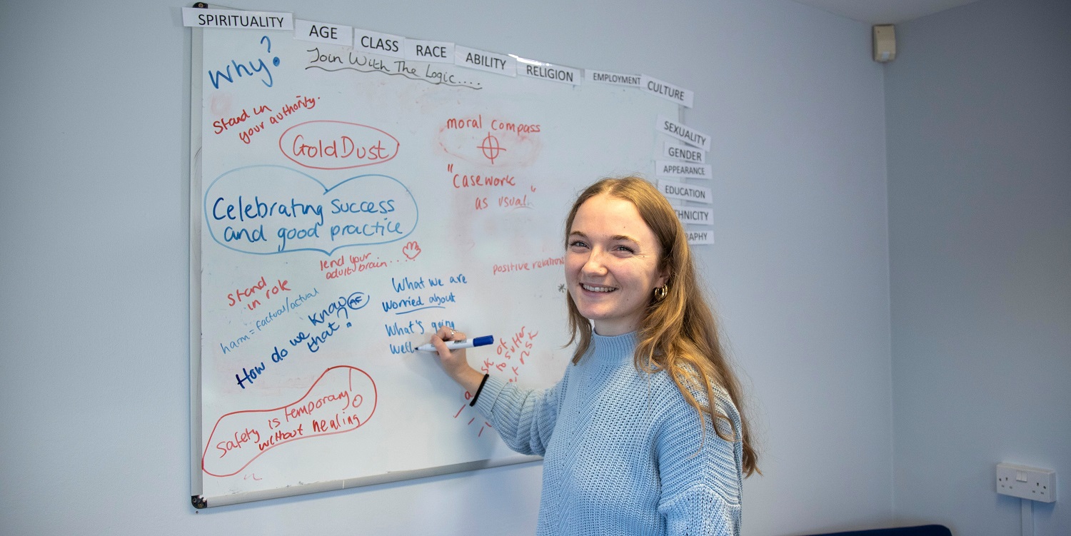 a young smiling woman writing on a whiteboard