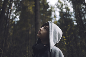 a teenage boy wearing a white hoodie and earphones looking up at trees