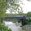 Side view of Bedminster bridge with a van driving across the bridge. The New Cut runs underneath the bridge and a line of different brighly coloured houses can be seen behind the bridge.