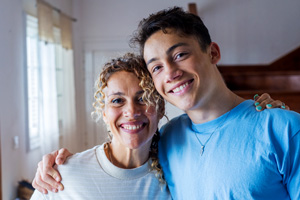 A young man and older woman stand side by side smiling at the camera.