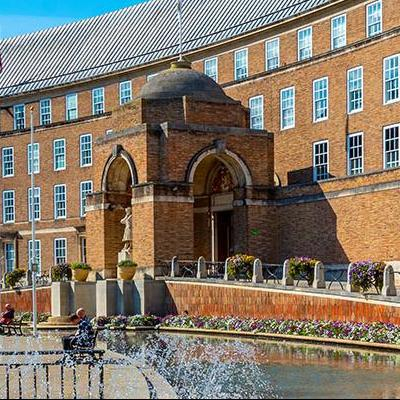 The outside of City Hall. A four storey red brick building with founains in front of the large ramp walkways leading up to the entrance.