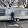 Man in a suit stood to the right of the door to his caravan.