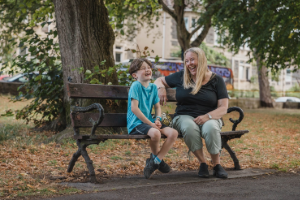 an adult and a child sitting on a bench chatting and laughing together