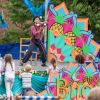 A juggler performing on a stage with a colourful backdrop and children watching in the audience