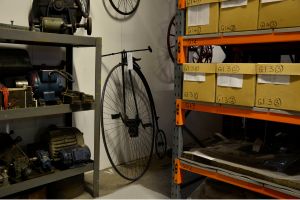 A store room in a museum with a penny farthing bicycle against wall.