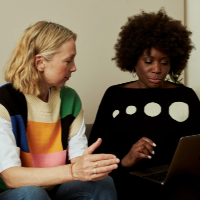two women on a sofa discussing something and looking at a laptop