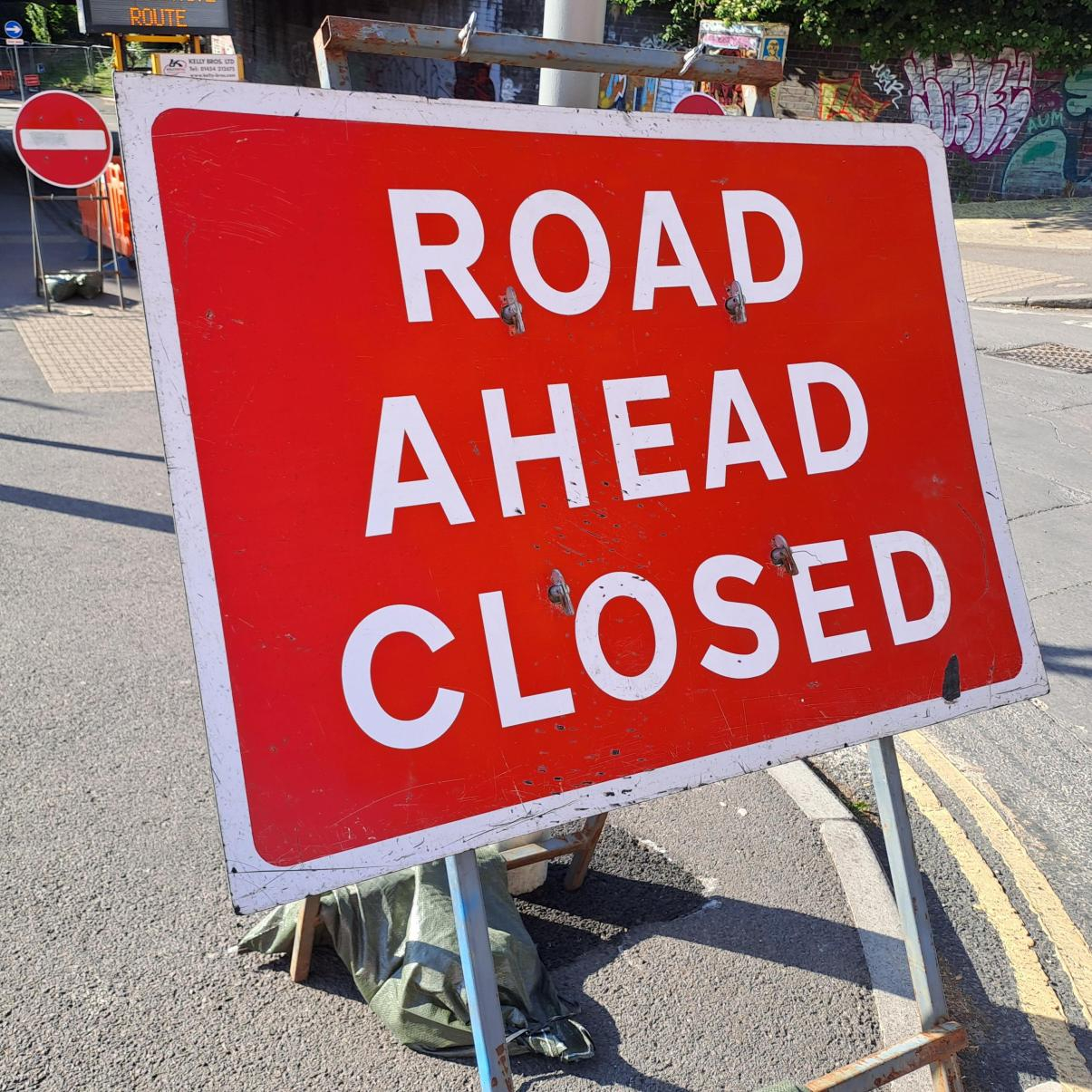 A red road sign which reads 'road ahead closed' placed on the corner or a pavement.