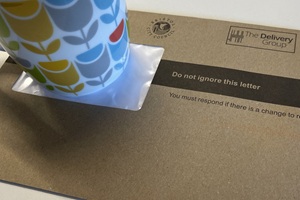 Postal letter on a desk with a mug nearby.
