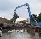 Crane with grabber pulling crushed van from crushing machine