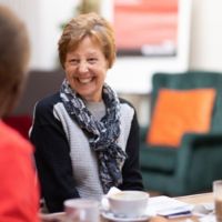 A smiling person seated talking to another person.