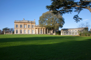 A view of a two storey stately house with long widows on a large green estate