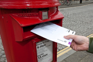 A letter is being posted into a red letterbox