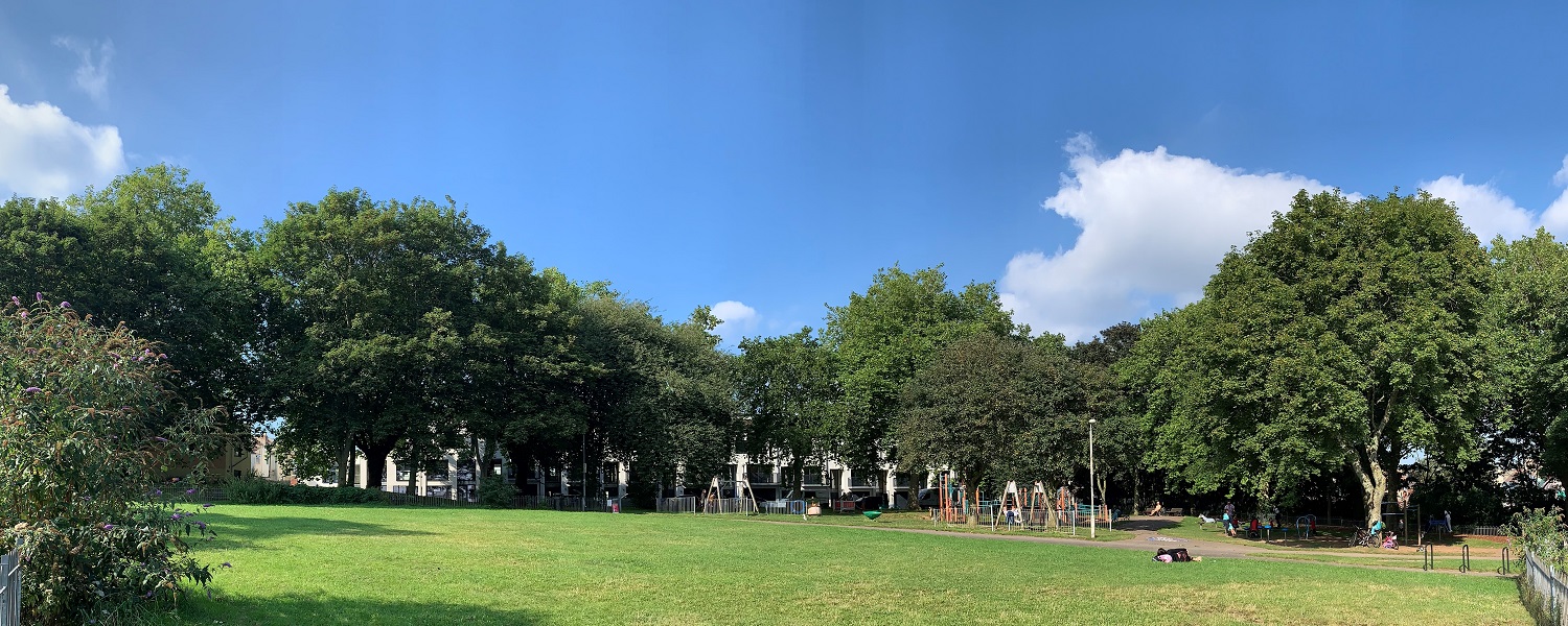 A children's play park in the middle of a larger park surrounded by trees