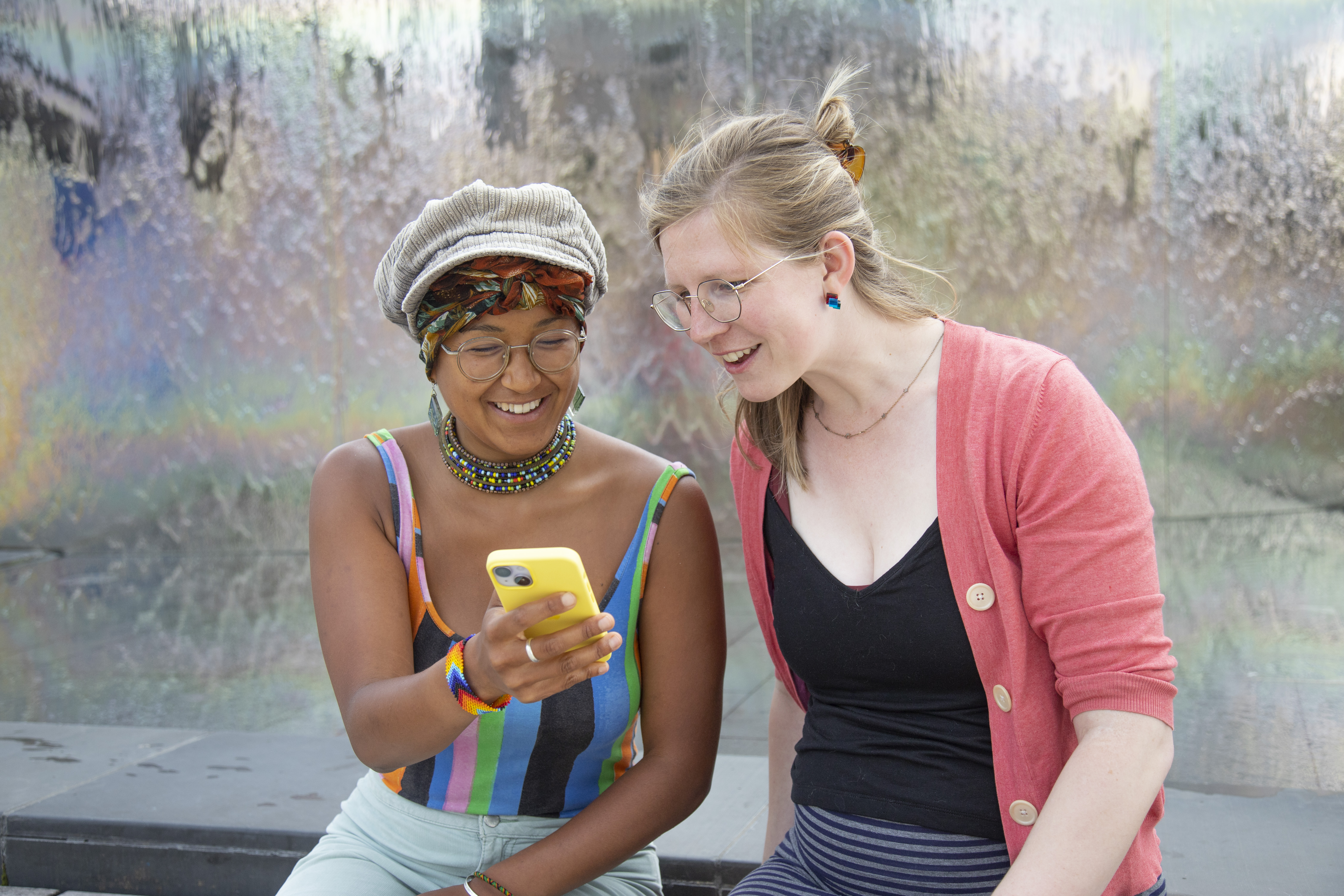 Two girls sitting on a wall looking at a yellow phone and smiling