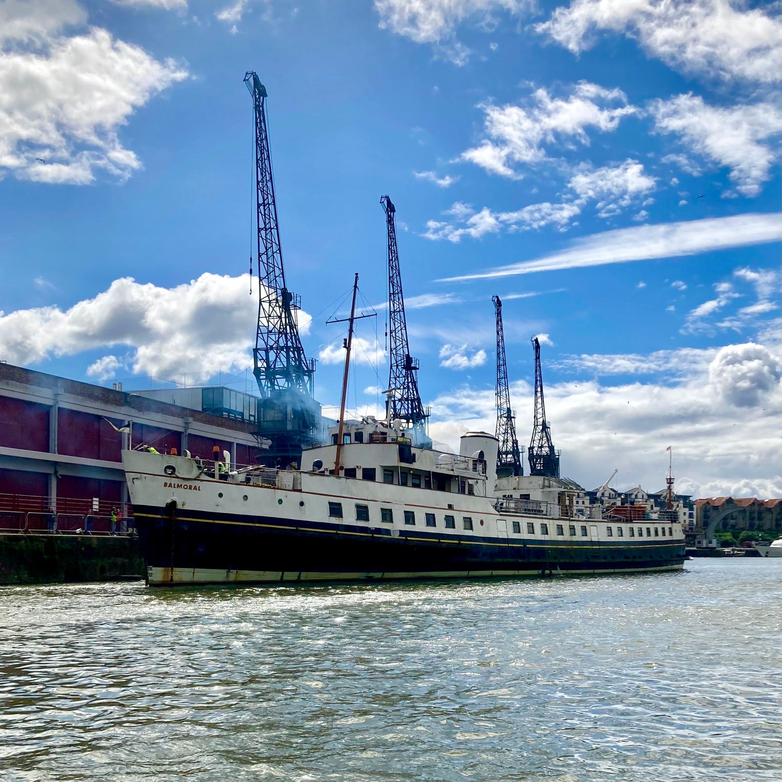 A big black and white boat on the water outside a red building, blue skies and white clouds