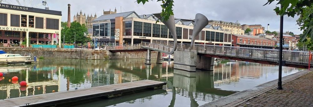 a bridge over the water with two grey horns on the side, waterfront bars in the background