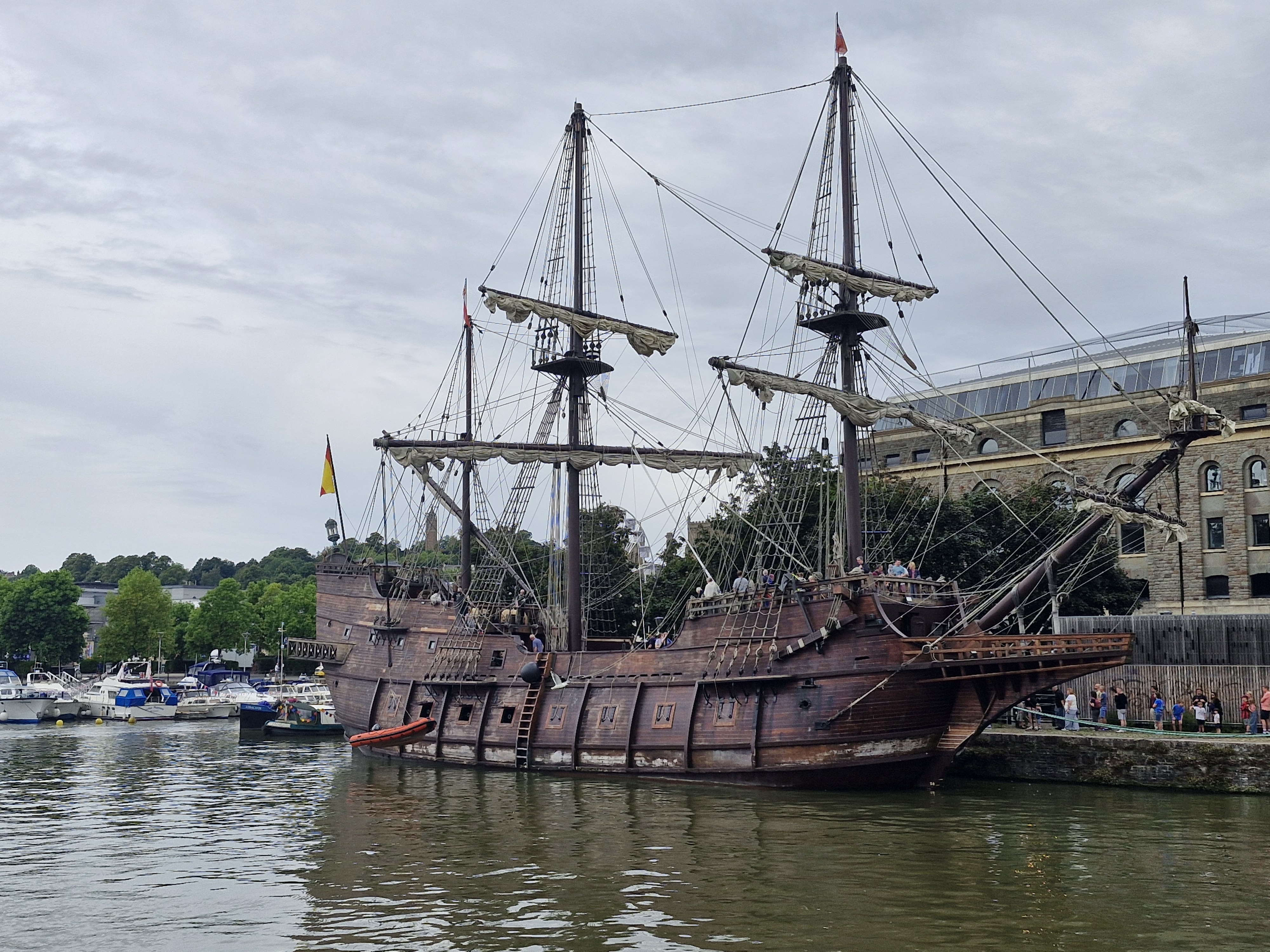 A big brown ship with tall masts and gun holes on the side, on the water