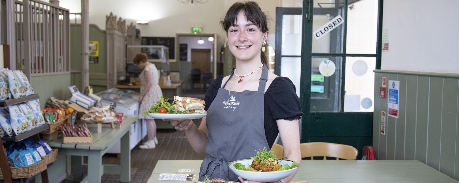 A member of staff holding plates of food inside the Courtyard Cafe