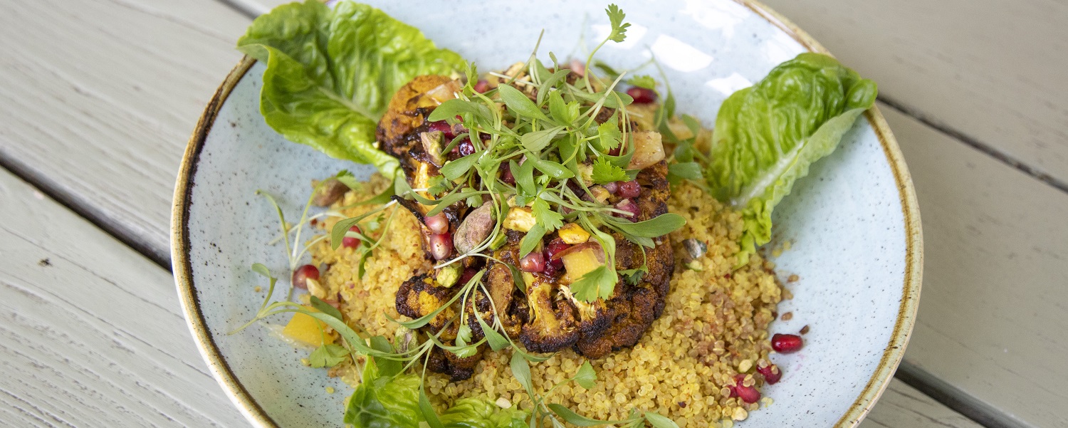 A bowl of cous cous, cauliflower, pomegranate seeds and lettuce