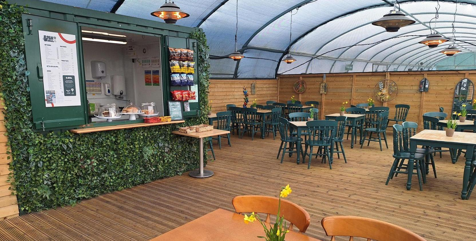 The Plant Cafe, showing tables and chairs inside a polytunnel like structure with plants dotted around.