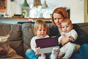 A woman with two babies in her lap looking at a tablet