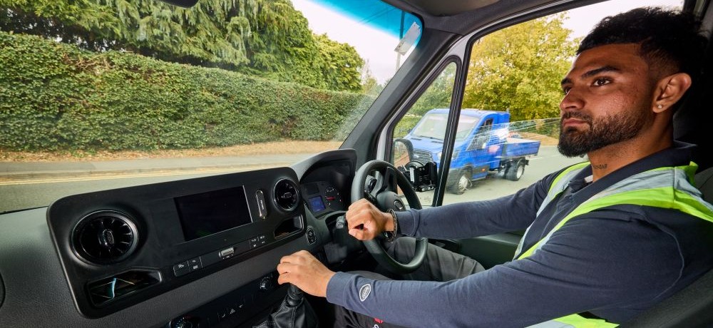 A man with a beard, wearing a high vis jacket, in the front seat of a van, looking out at the road.
