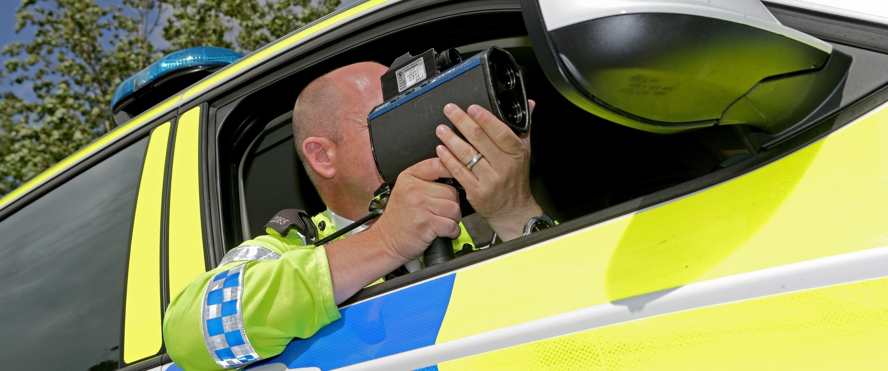 A man in an enforcement vehicle, pointing a speed camera out of the window