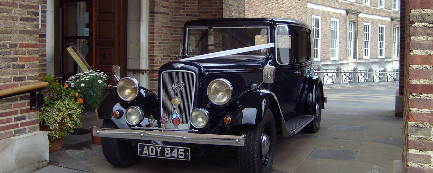 A black classic car with a white ribbon across the bottom of the windscreen parked by City Hall