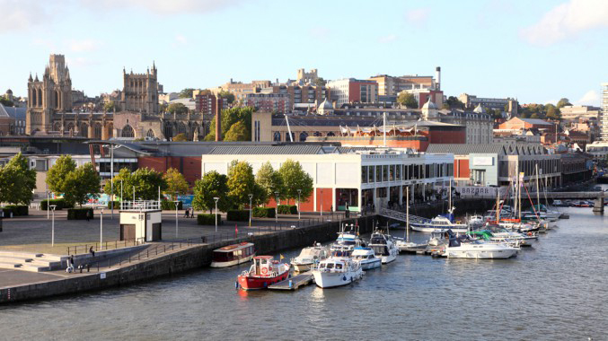 A view of Bristol Floating Harbour with M shed in the foreground and the cathedral in the background