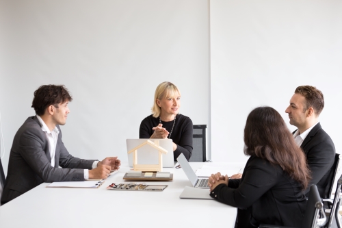 Colleagues sitting around a table with laptops and a wooden house symbol in the middle