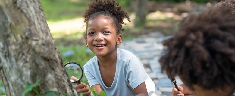 Children having fun with magnifying glasses outside in nature.