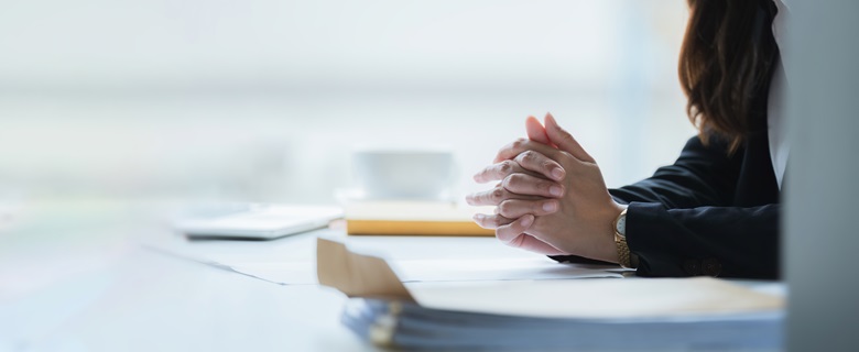 Someone making an important decision with their hands interlocked resting their arms on paperwork.