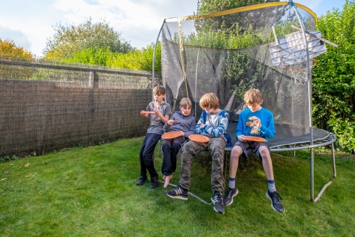 Young boys sitting on a trampoline in a garden whist eating pizza