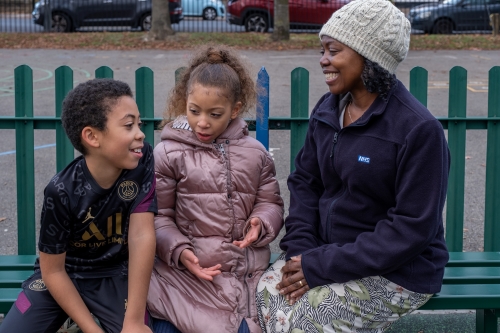 Carer with a boy and a girl sitting on a park bench