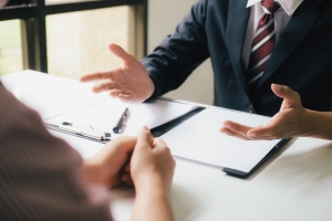 Two people sitting opposite each other at a desk with one giving advice
