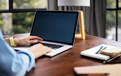 Person sitting at a desk with their hands on the keyboard of an open laptop with a blank screen