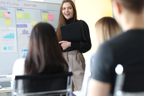 Woman speaking in front of a group of colleagues while standing in front of a whiteboard