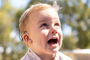 A laughing toddler with a hearing aid
