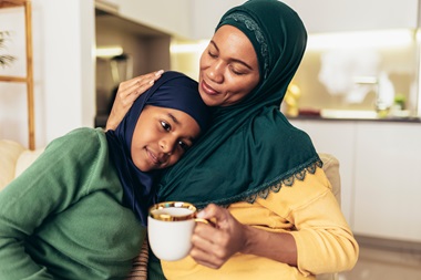 A mother holding a cup of tea and embracing her child