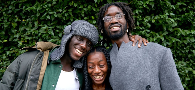 3 people with their arms around each other, smiling. 