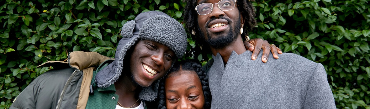 Three people laughing and smiling together in a green and leafy area.
