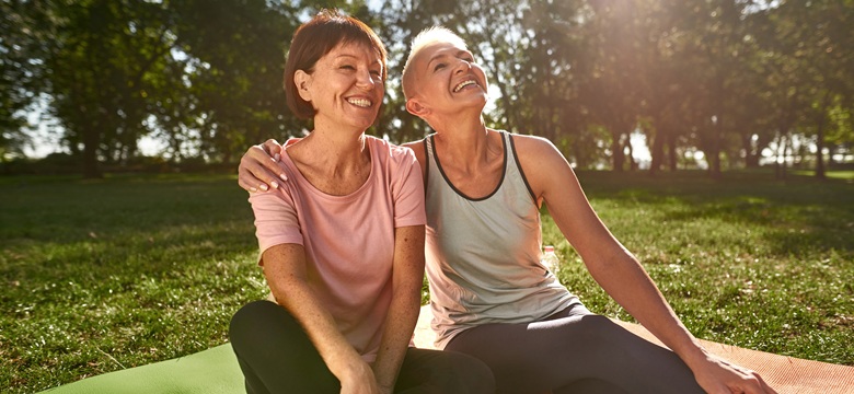 2 ladies sat on a picnic blanket enjoying the sun in a park