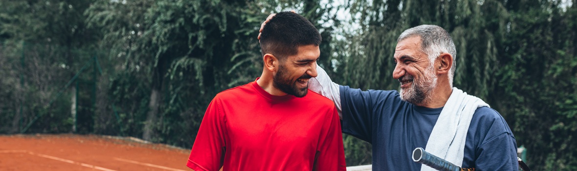 Two people laughing together on court having played tennis.