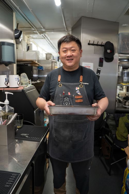 A man wearing an apron, holding a baking tin