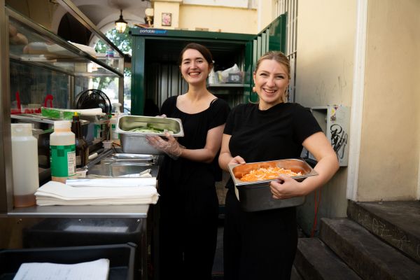 Two employees holding some trays containing food and smiling
