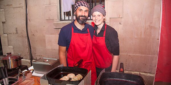 A man and a lady smiling in front of a pan cooking dumplings