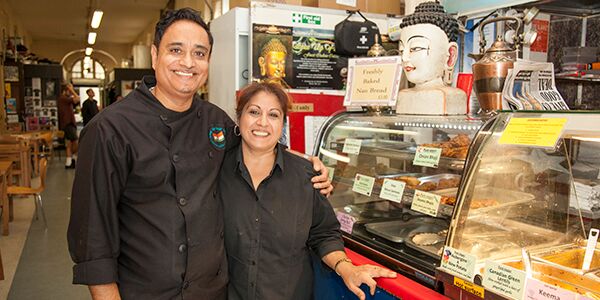 A man and a lady smiling in front of their shop